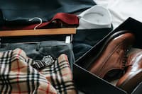 Outfit laid out including a suit, dress shirt, tie, wristwatch, plaid scarf, and brown dress shoes in a box.