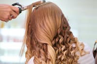 Close-up of a hairdresser using a curling iron to style a woman's long, blonde hair