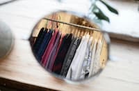 Reflection of various sweaters and garments hanging on a rack, seen through a circular mirror